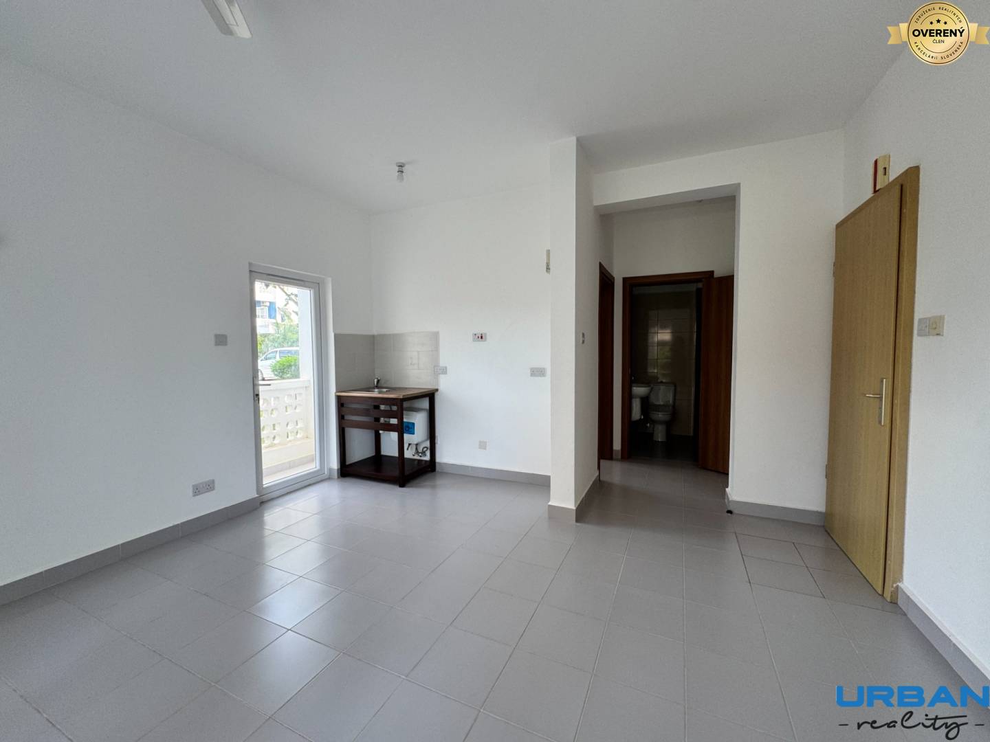 Svetlá miestnosť v 2-izbovom byte s balkónovými dverami, kachľovou podlahou a vstupom do kúpeľne.