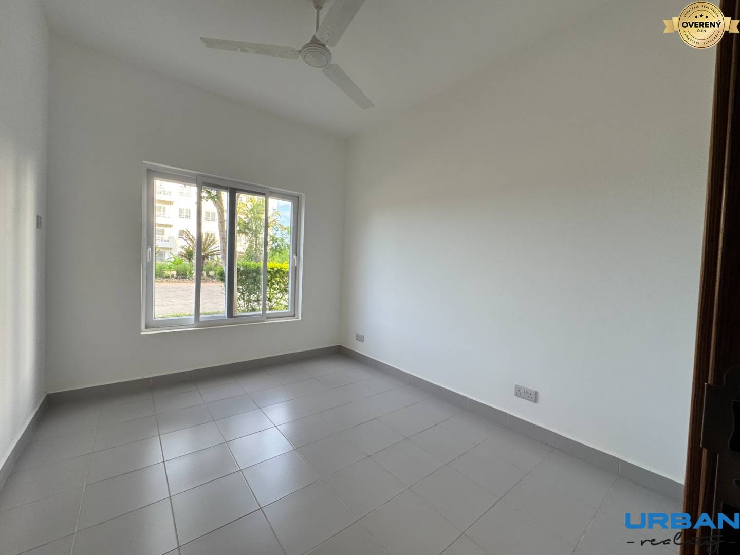 Miestnosť s bielymi stenami, dlažbou a veľkým oknom v 2-izbovom byte.